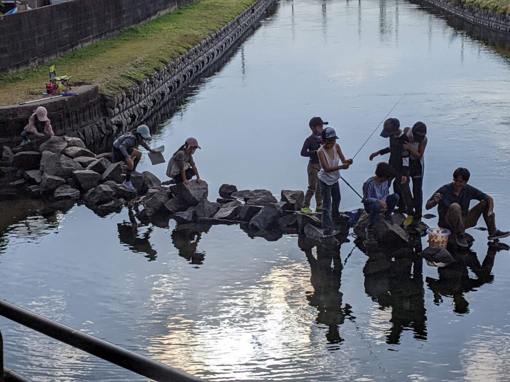川で魚釣りをしている大人と子ども。